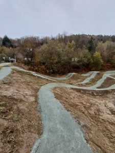 Ein gewundener Feldweg mit Serpentinen führt durch einen kargen, schlammigen Hang, umgeben von blattlosen Bäumen und dichtem Wald unter einem grauen, bedeckten Himmel – eine perfekte Szene für Mountainbike-Bewegungsbegeisterte.